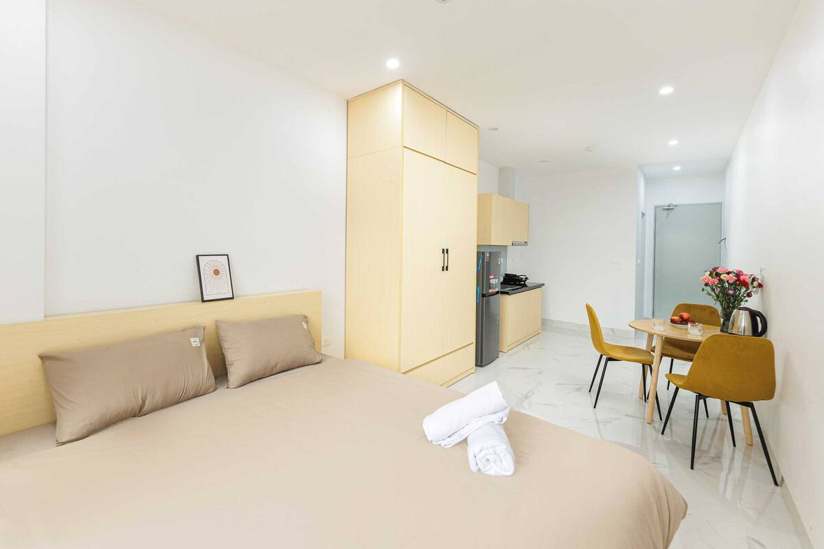 A hotel room with a bed, a wardrobe, a kitchenette, a dining area with chairs, and a small table.
