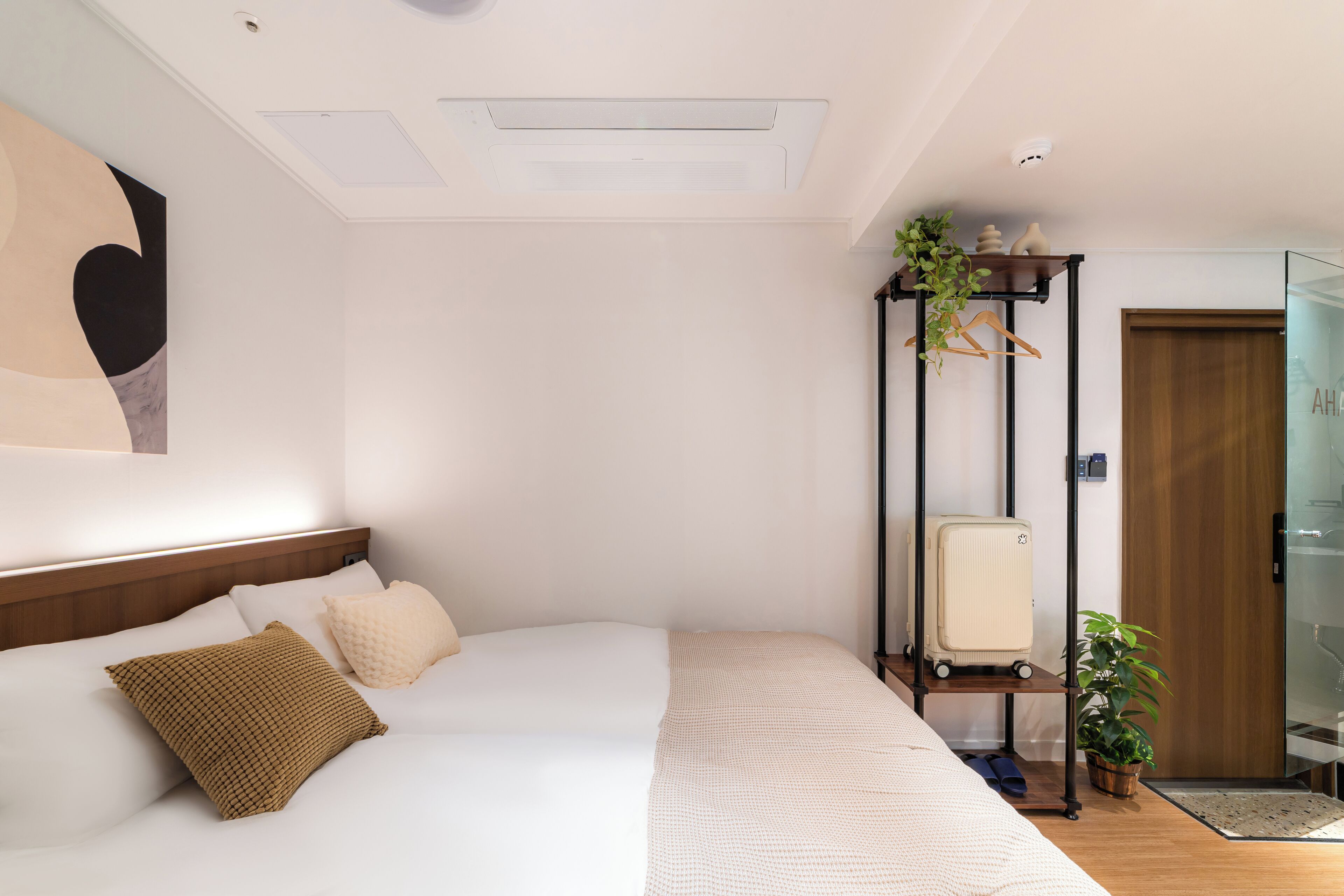 Una habitación de hotel con una cama, una planta colgante, una maleta y una puerta de madera.