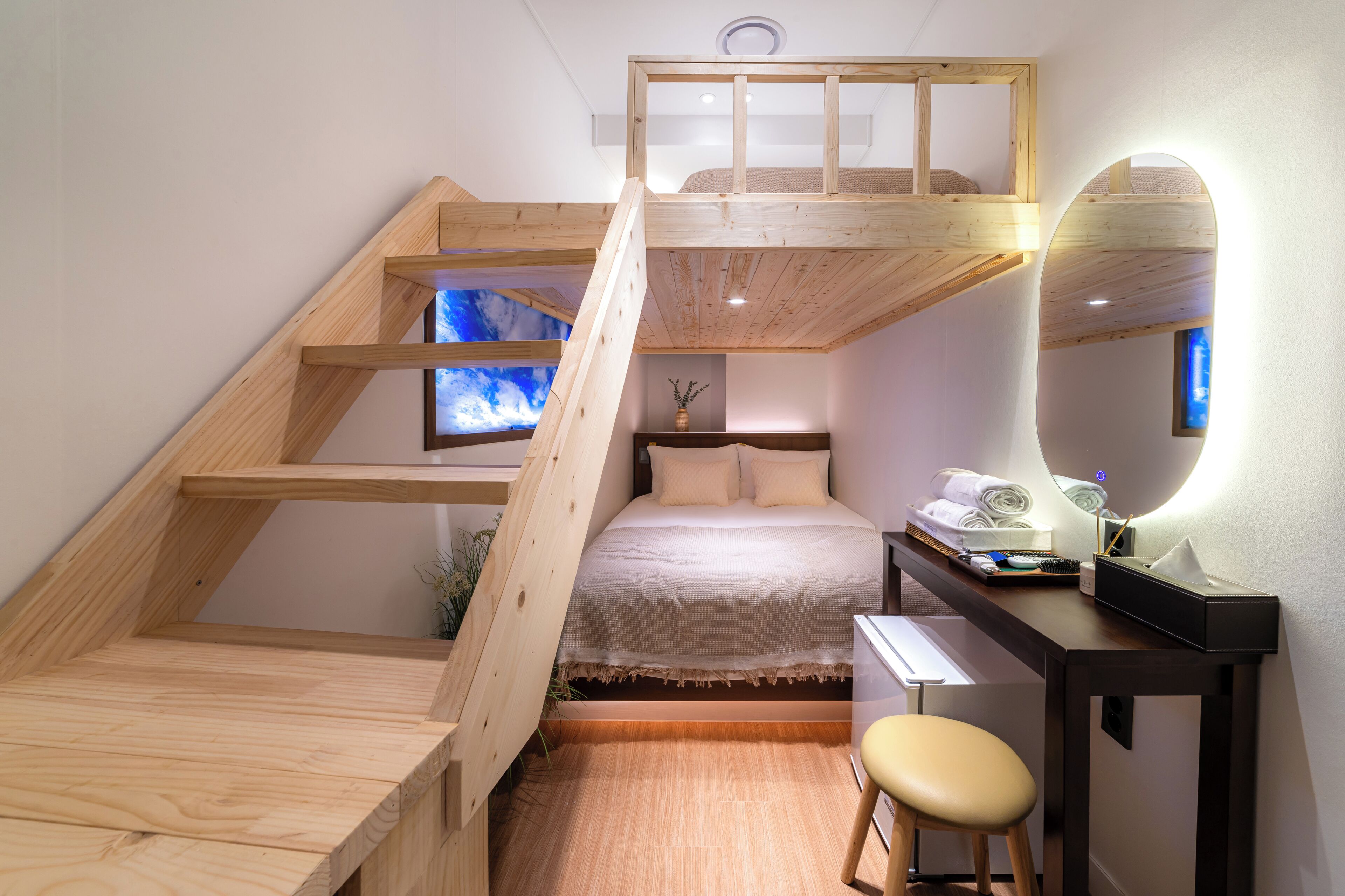 Un dormitorio compacto con literas, un escritorio con silla, un espejo y una ventana pequeña.