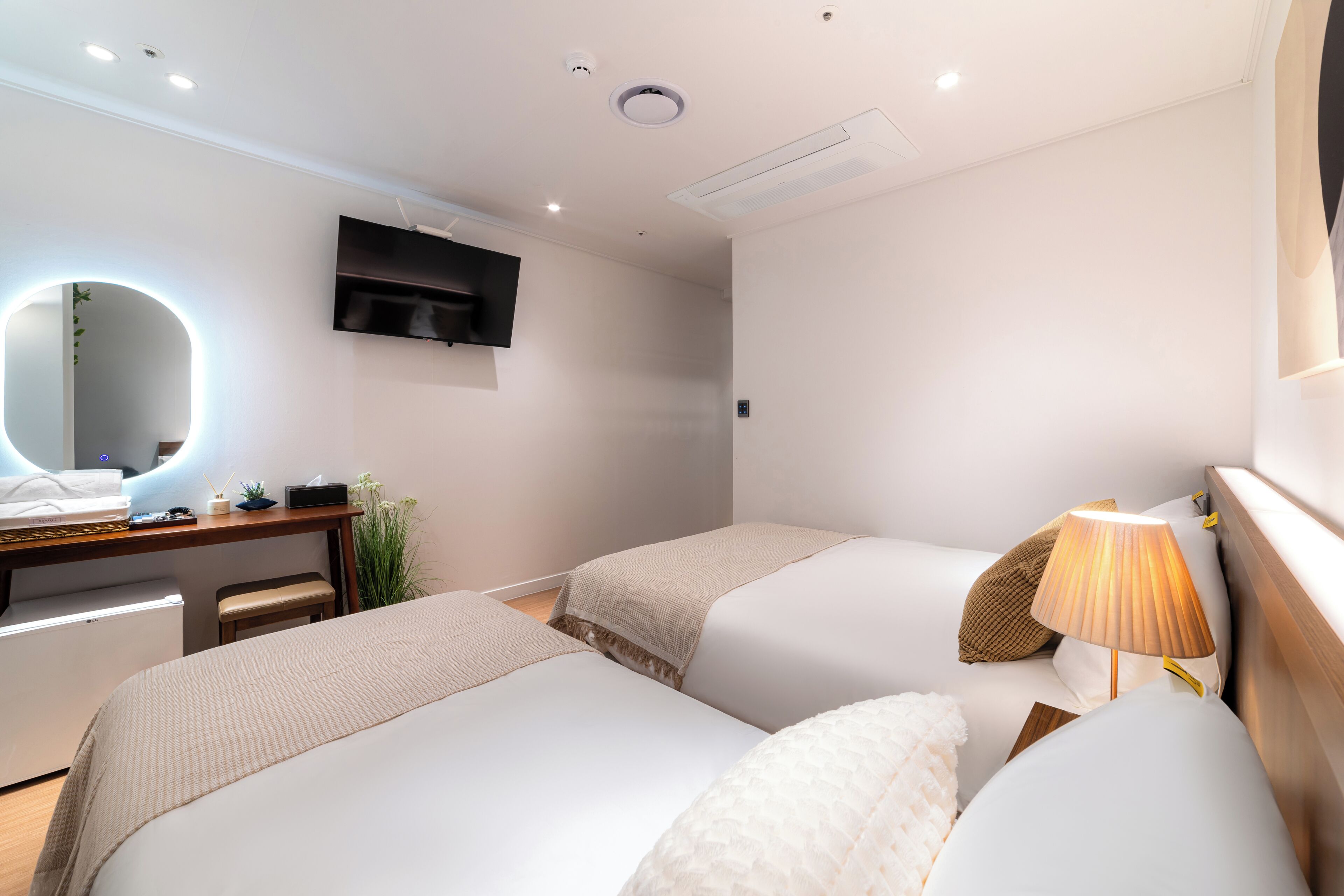 Una habitación de hotel con dos camas, un escritorio con silla, televisor y espejo.