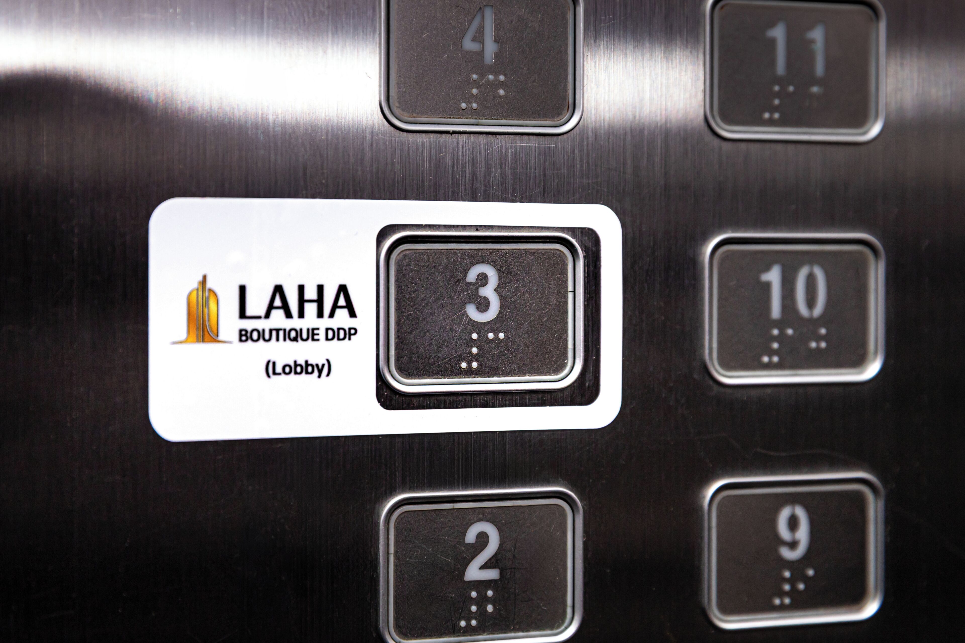 Et elevatorpanel med knapper til valg af etage, inklusive en knap mærket 'LAHA BOUTIQUE DDP (Lobby)'.