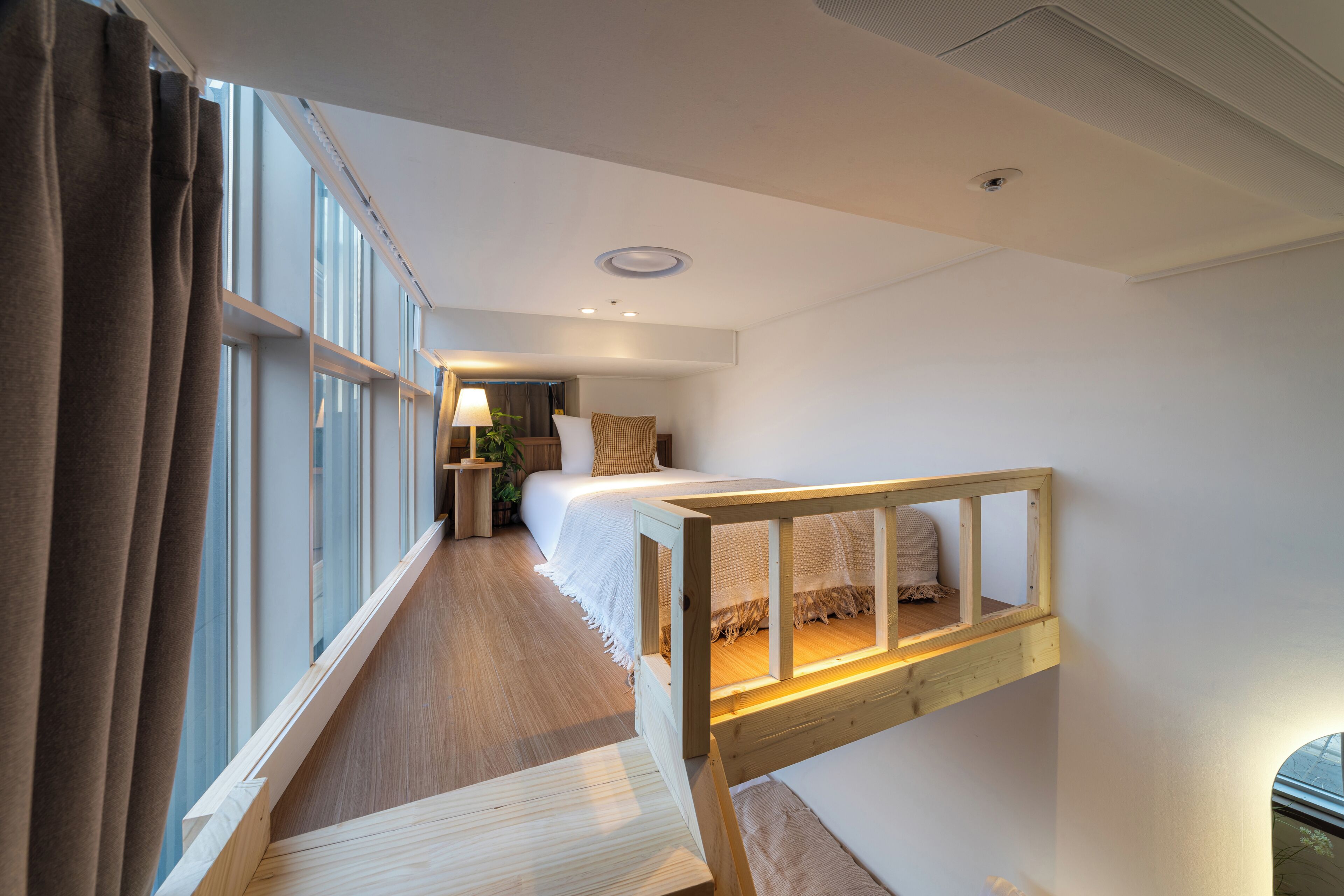 A hotel room with a bunk bed, a bedside table, a lamp, and a window with curtains.