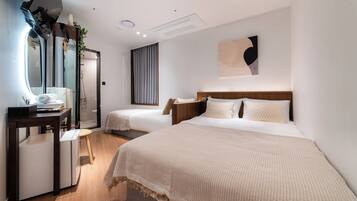 A hotel room with a large bed, a smaller bed, a desk with a chair, a mirror, and a wall-mounted artwork.