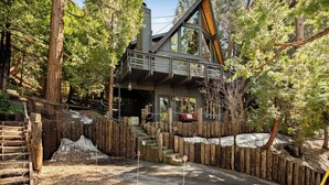 A cabin with a wooden deck, a staircase leading to a second level, and a surrounding wooden fence.