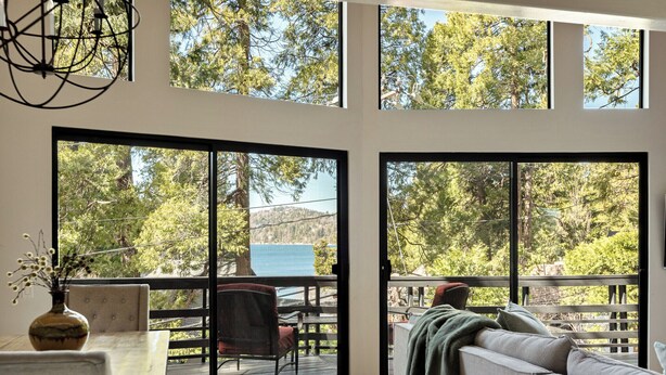 A room with a large sliding glass door leading to a deck, a sofa, a table, and a vase with flowers.