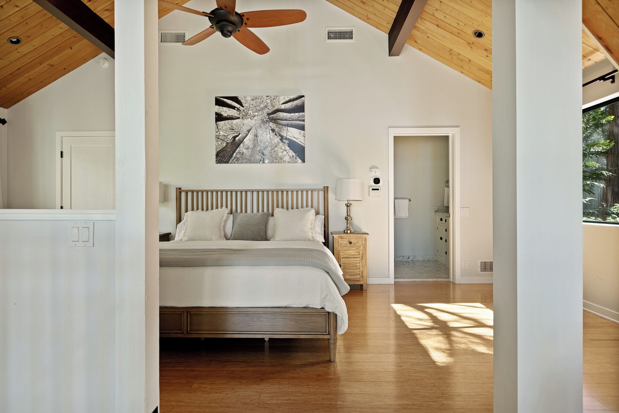 Un dormitorio con cama, ventilador de techo, mesita de noche, lámpara de pared y una puerta que da a otra habitación.