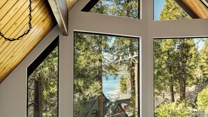 A room with large windows, wooden ceiling beams, and a view of a forested area.