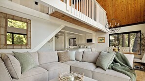 A modern living room with a sectional sofa, a coffee table with a decorative item, a staircase, and a view of the outdoors.