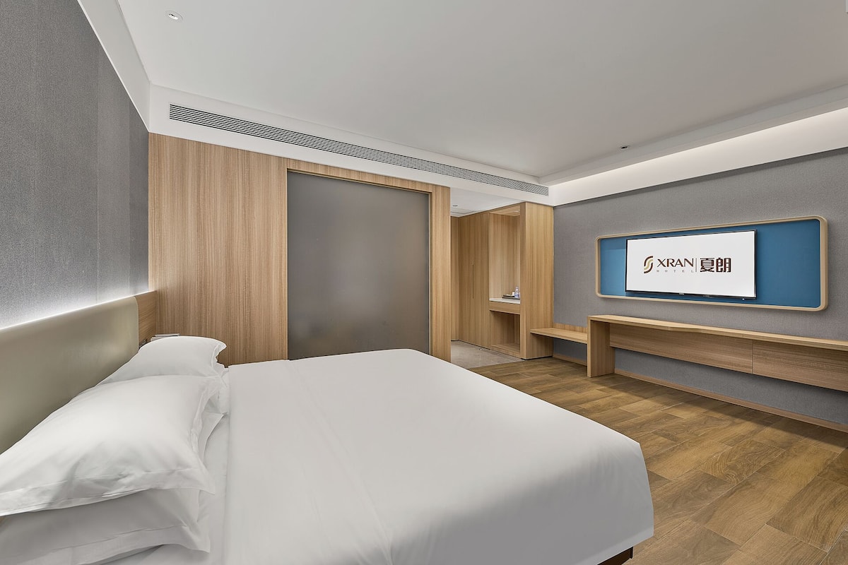 A modern hotel room with a bed, a TV mounted on the wall, and a wooden wardrobe.