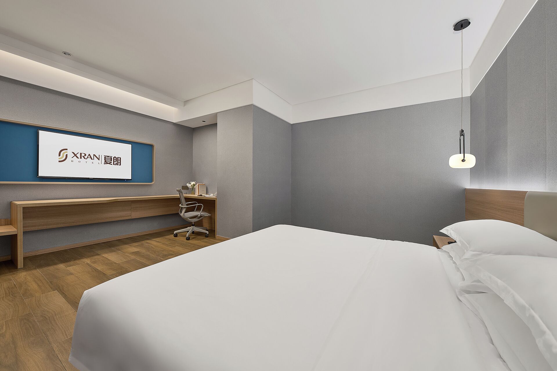 A hotel room with a bed, a desk, a chair, a nightstand, and a wall-mounted TV.