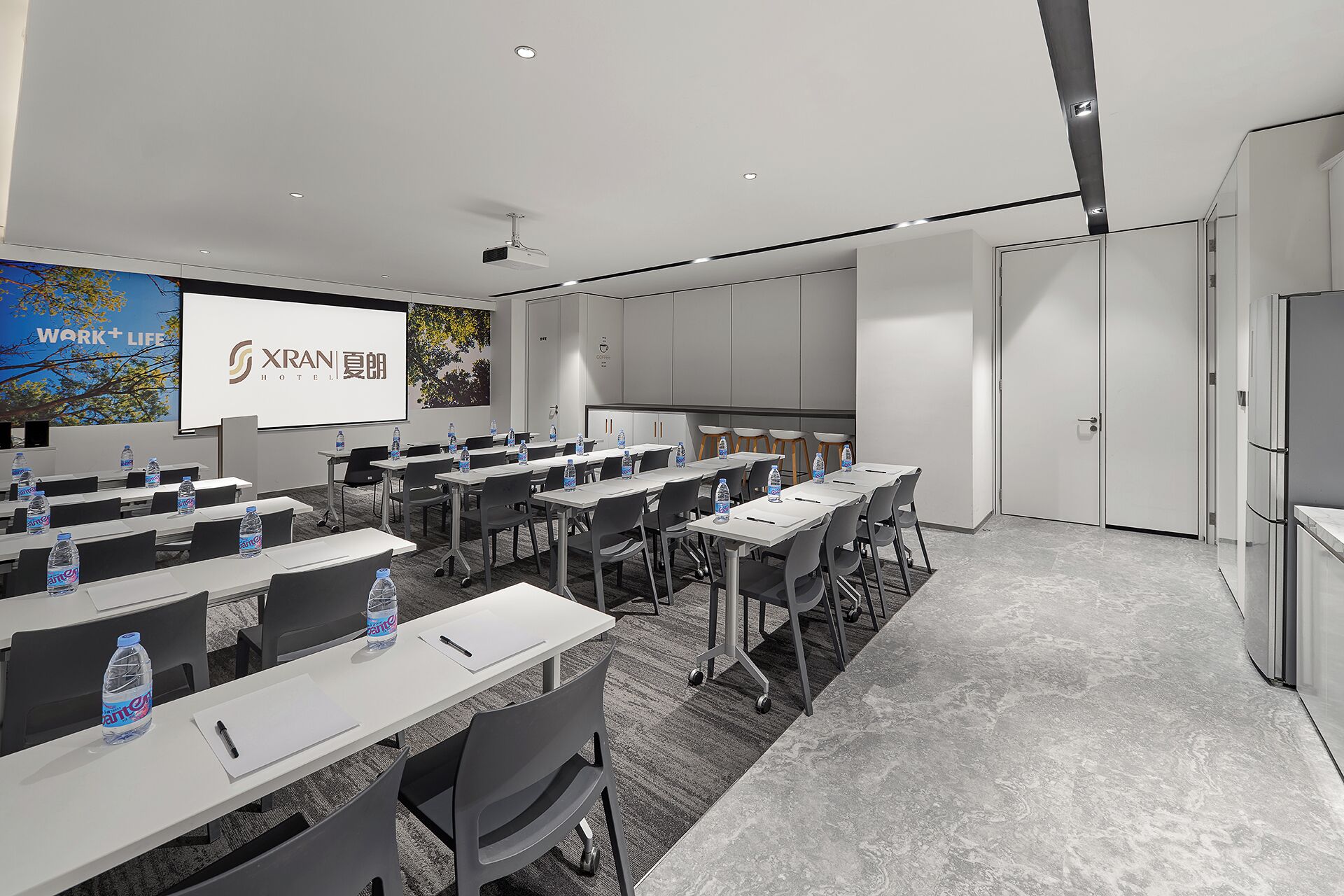 A conference room with tables, chairs, water bottles, a projector screen, and a presentation on the wall.