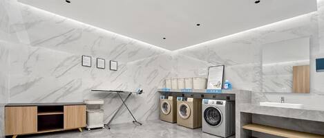Een moderne badkamer met marmeren wanden, een wastafel, een spiegel en een aantal wasmachines.