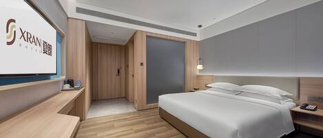 A modern hotel room with a bed, bedside table, TV, and wooden flooring.