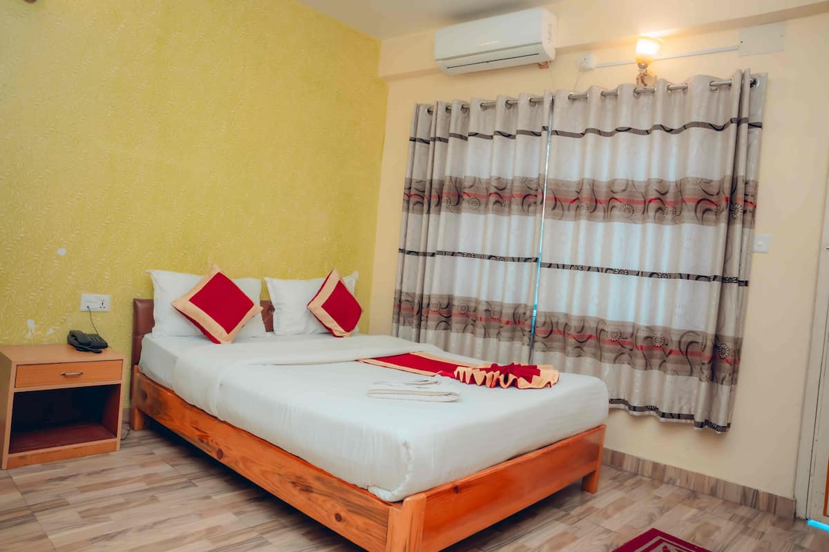 A bedroom with a wooden bed, a nightstand, a wall-mounted air conditioner, and a window with patterned curtains.
