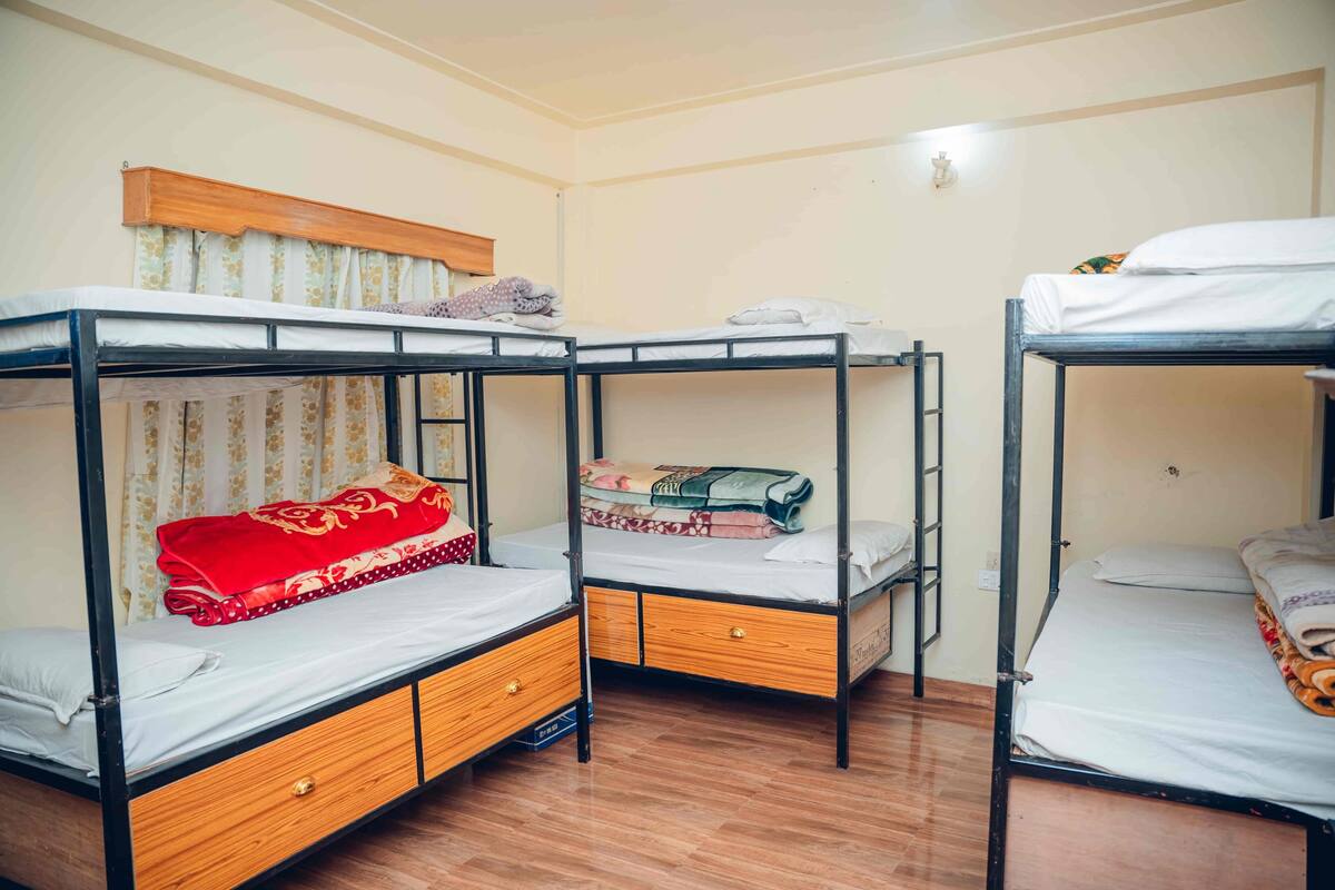 A room with three bunk beds, wooden drawers, a wooden headboard, and a curtain.