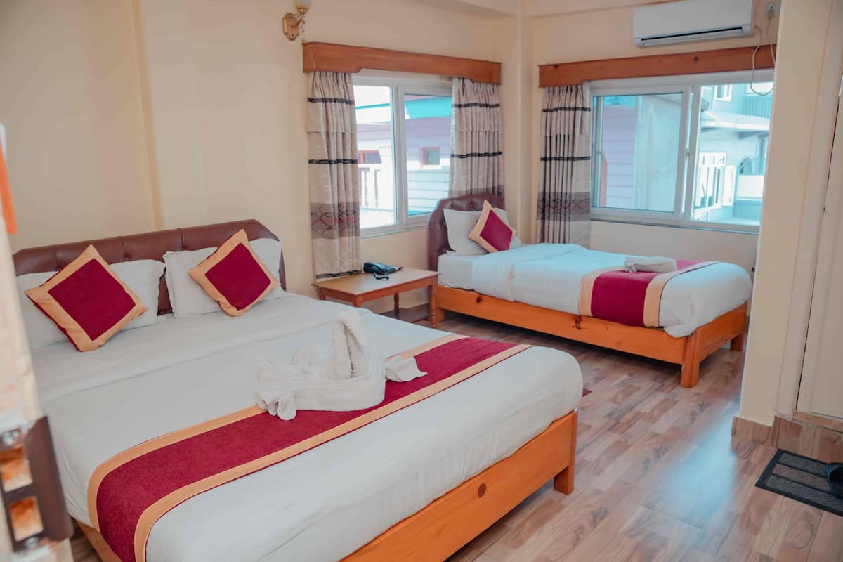 A hotel room with two beds, wooden headboards, a bedside table with a phone, and a window with curtains.