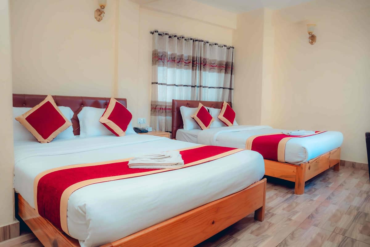 A hotel room with two beds, a wooden headboard, a red and white bedspread, a curtain, and a wall-mounted light fixture.