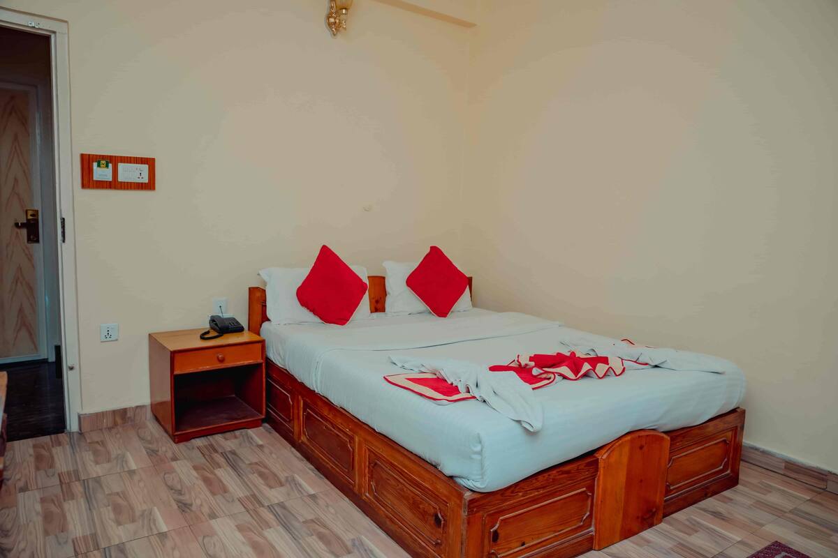 A bedroom with a wooden bed, red pillows, a nightstand, and a telephone.