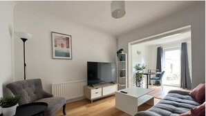 A modern living room with a sofa, a TV, a dining table, and a plant. - Eye Road Retreat (Peterborough)