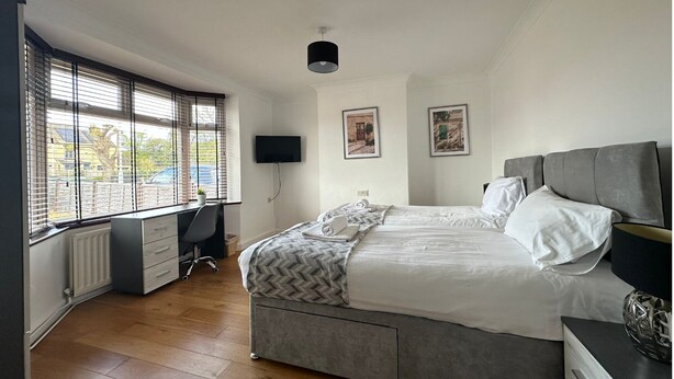 A bedroom with a bed, a desk, a chair, a TV, and two framed pictures on the wall. - Eye Road Retreat (Peterborough)