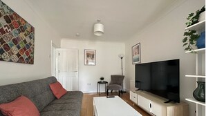 A modern living room with a grey sofa, white coffee table, and a large flat-screen TV. - Eye Road Retreat (Peterborough)