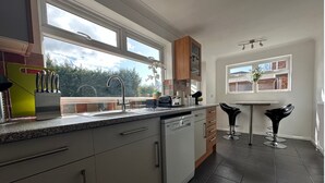A modern kitchen with a dishwasher, a window, and a bar area with stools. - Eye Road Retreat (Peterborough)