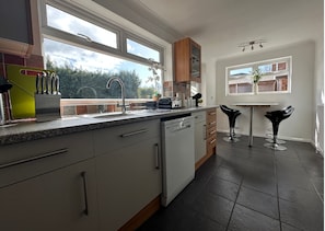 A modern kitchen with a dishwasher, a window, and a bar area with stools. - Eye Road Retreat (Peterborough)