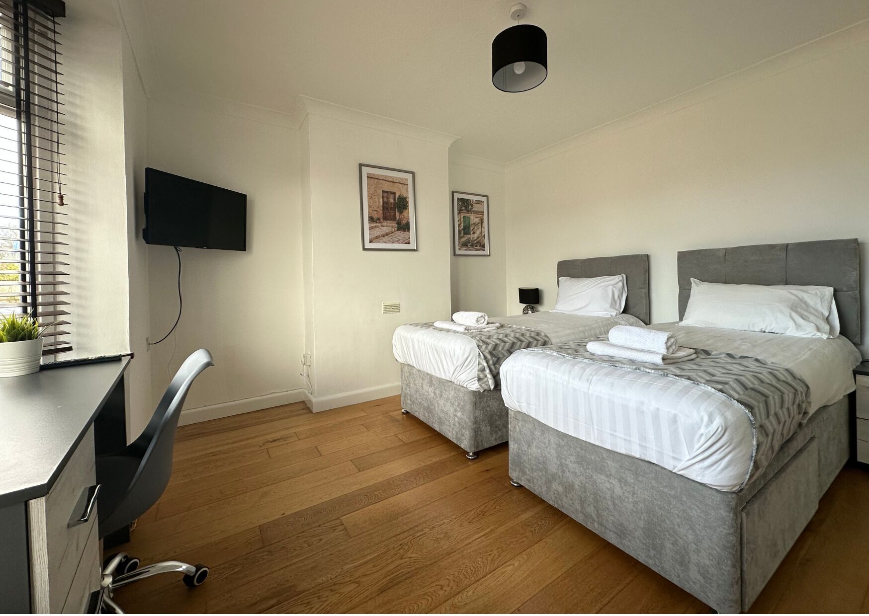 Une chambre d’hôtel avec deux lits, un bureau, une chaise, une télévision et des œuvres d’art accrochées au mur.