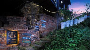 Un edificio de ladrillo con varios letreros, una escalera y un muro de ladrillo con plantas.