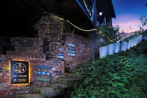 A brick building with multiple signs, a staircase, and a brick wall with greenery.