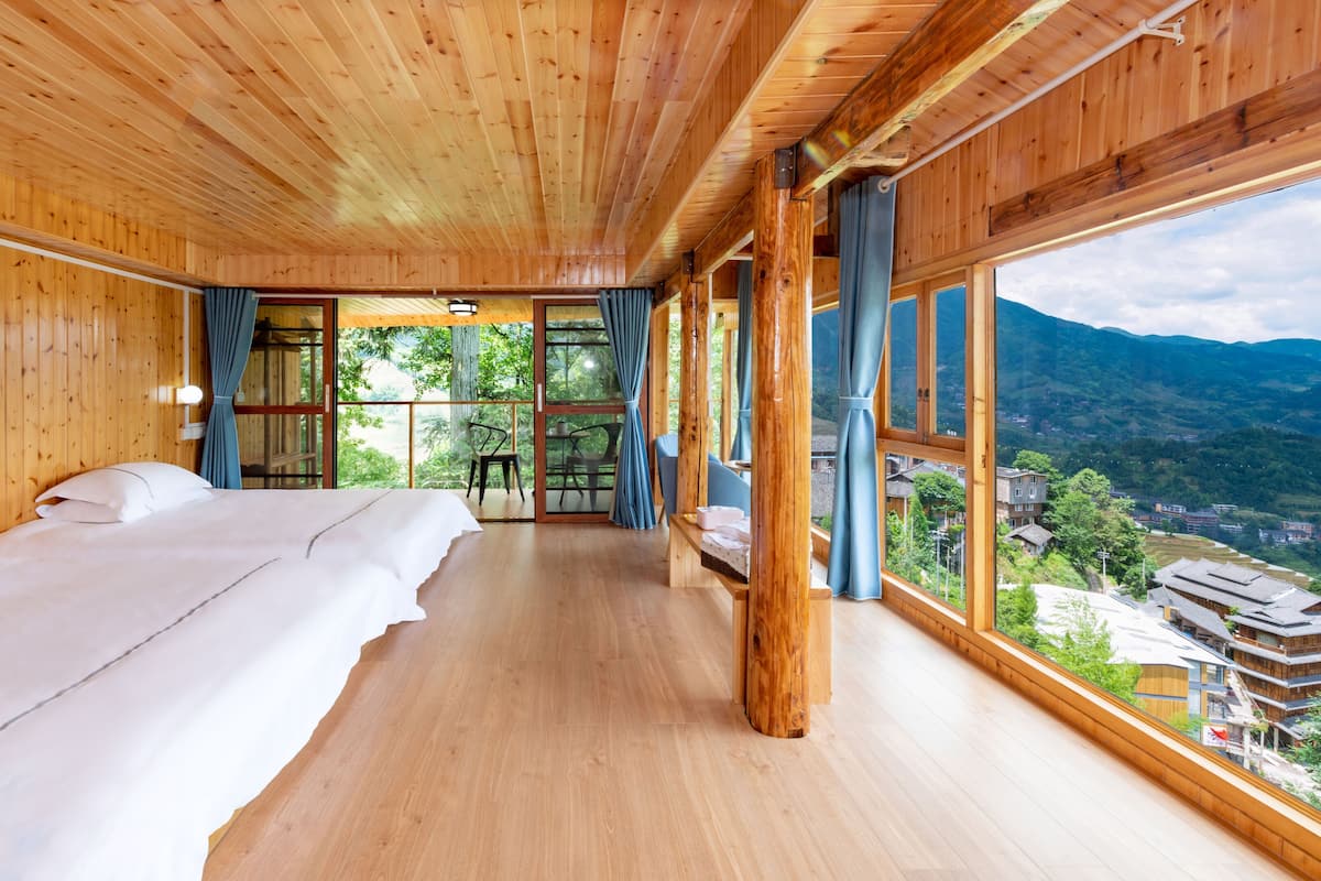 Un interior de madera con una cama, una mesa y vistas a un paisaje montañoso.
