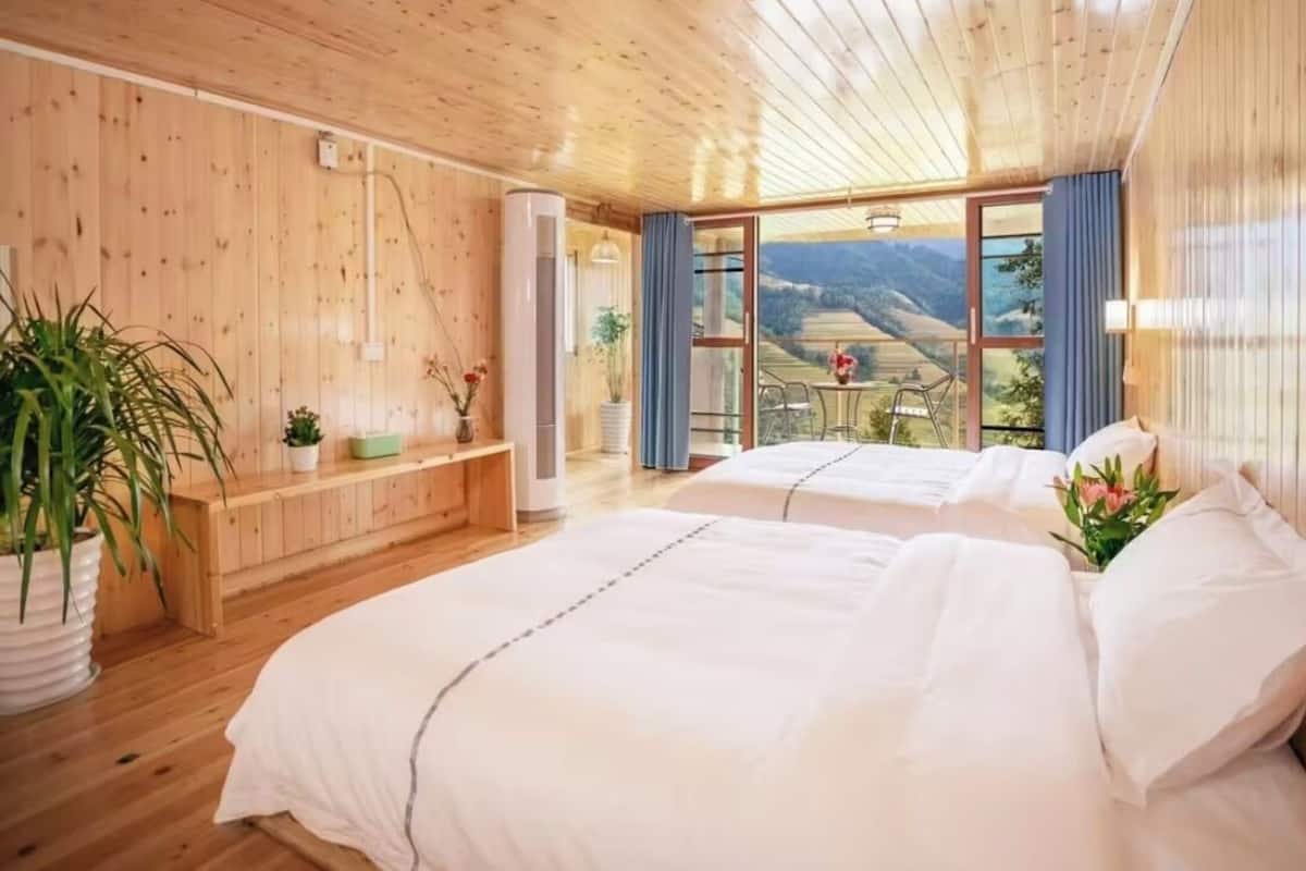 Una habitación con paneles de madera, dos camas, un banco y vistas al exterior.