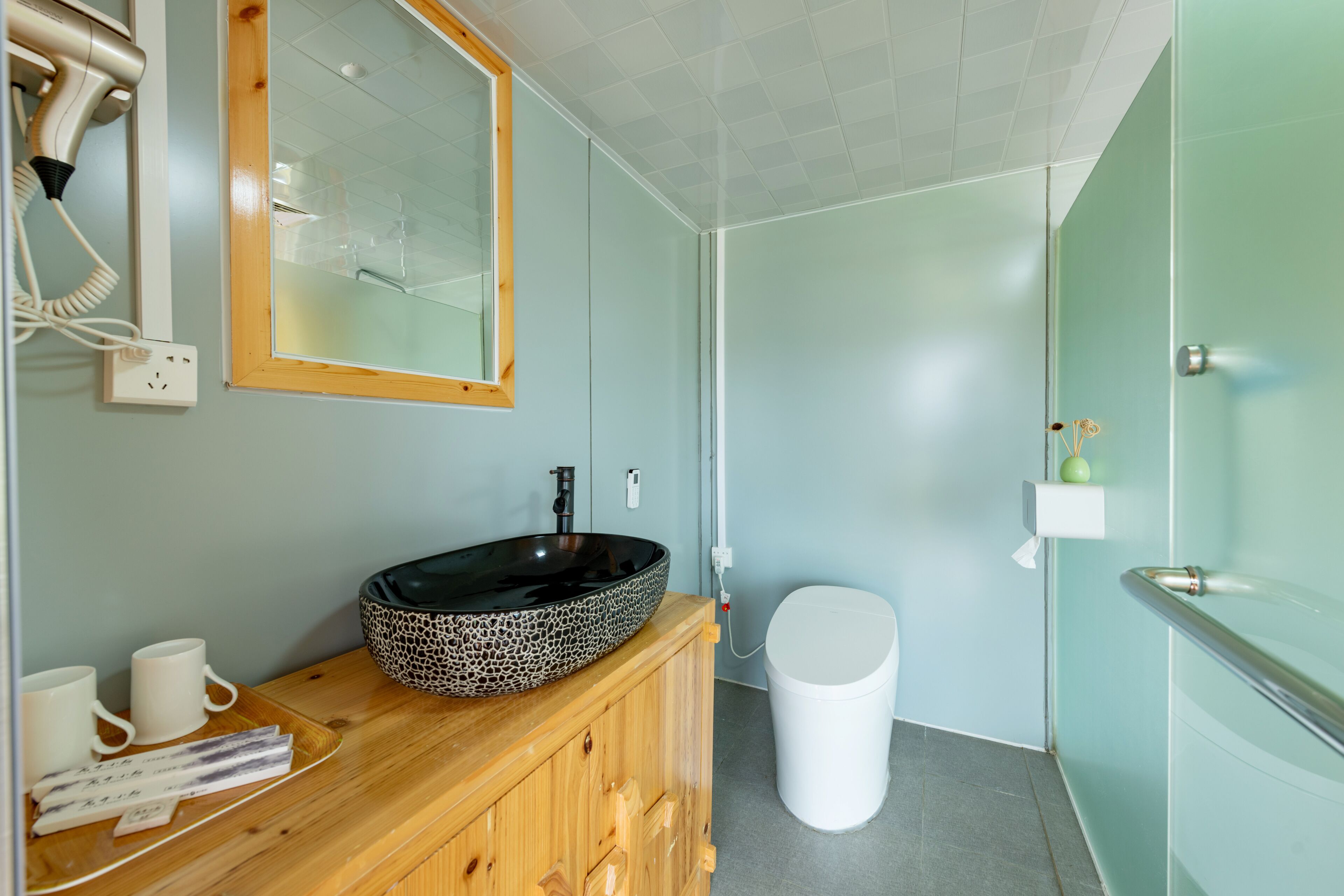 Une salle de bain avec un meuble-lavabo en bois, un lavabo sur colonne noir, des toilettes blanches et un miroir au-dessus du lavabo.