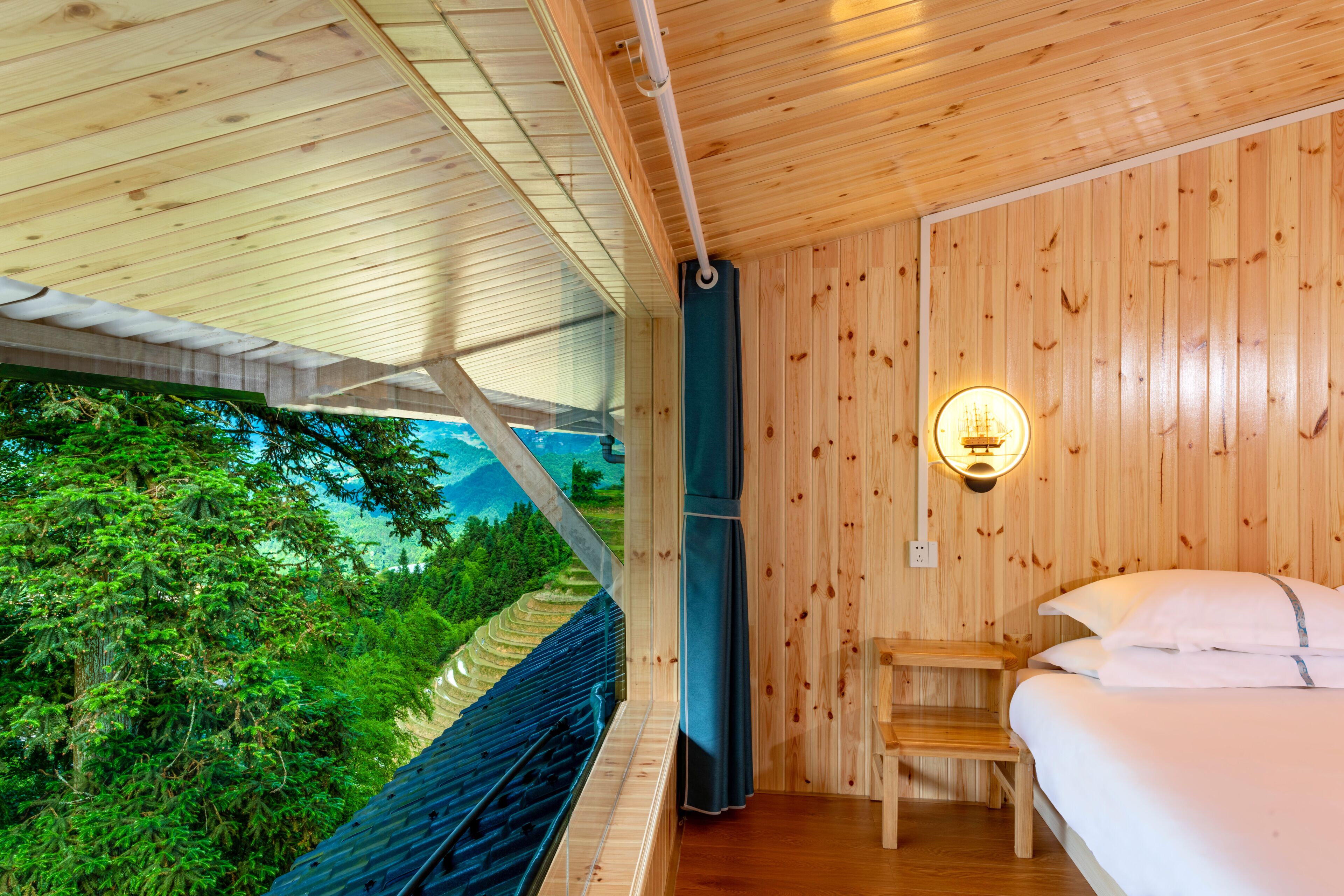 Een houten hutje met een bed, een bank en uitzicht op een bebost gebied.