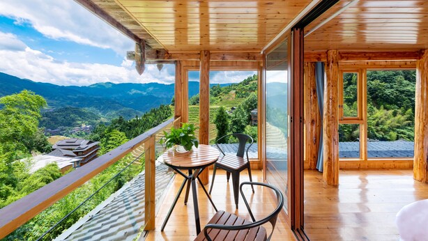 Una terraza de madera con una mesa y sillas, con vistas a un paisaje montañoso.