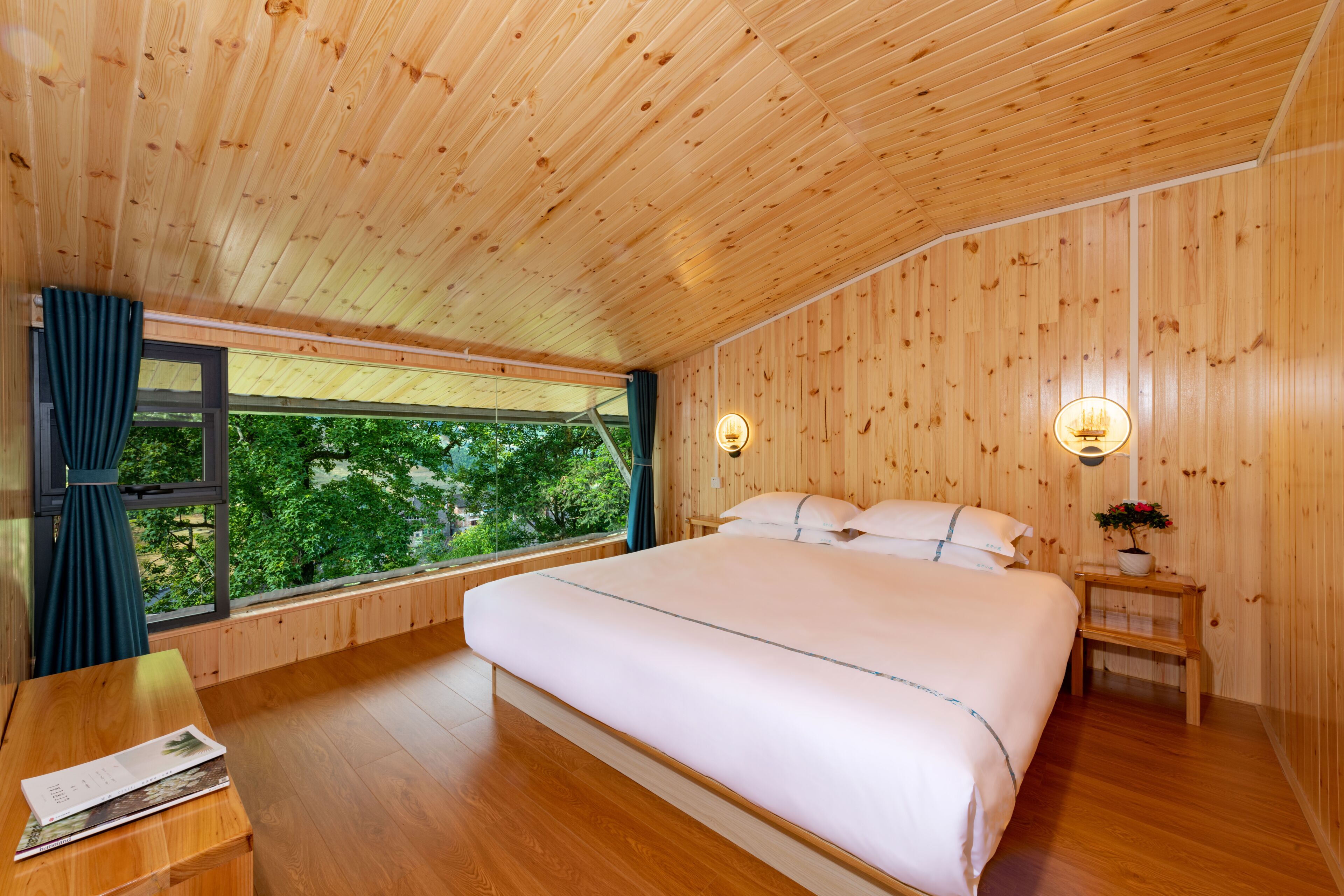 A bedroom with a wooden ceiling, a large bed, a window with curtains, and a bedside table with a lamp.