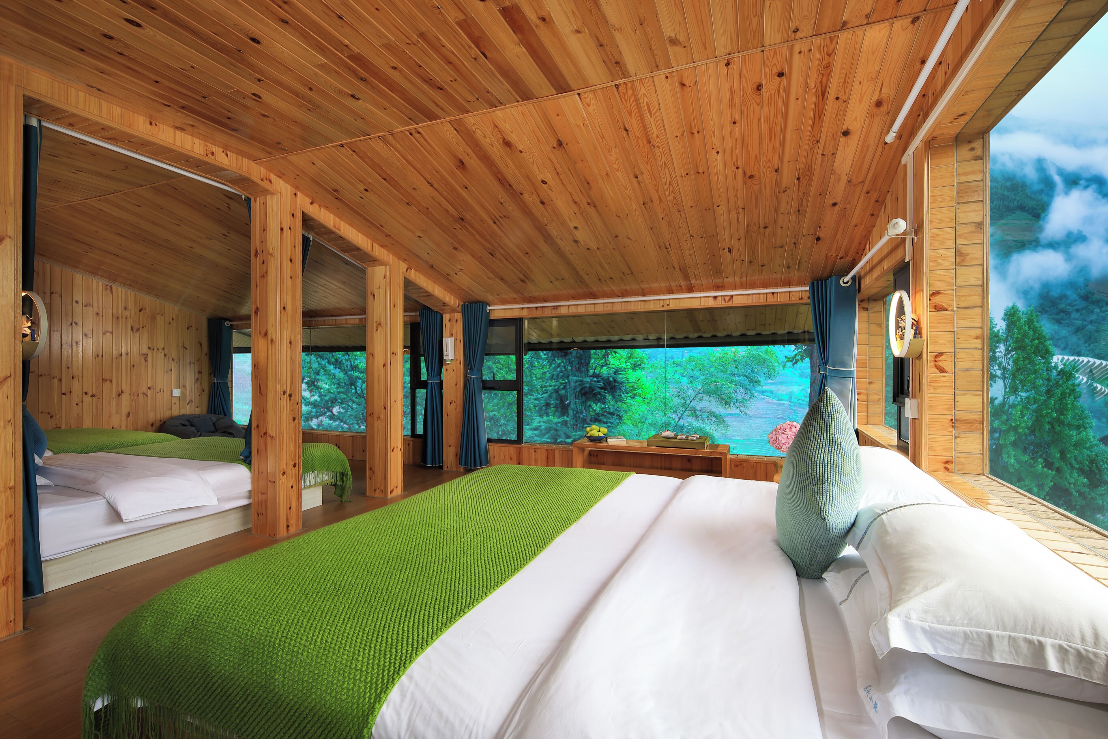 Una cabaña de madera con una cama grande, una cama más pequeña y vista al bosque a través de una ventana.