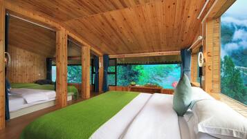 Una cabaña de madera con una cama grande, una cama más pequeña y vista al bosque a través de una ventana.
