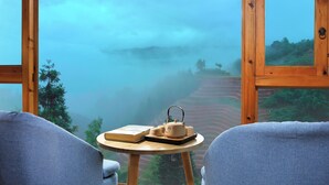 Habitación con vista a un paisaje brumoso, una mesa redonda pequeña con una tetera y dos sillas.