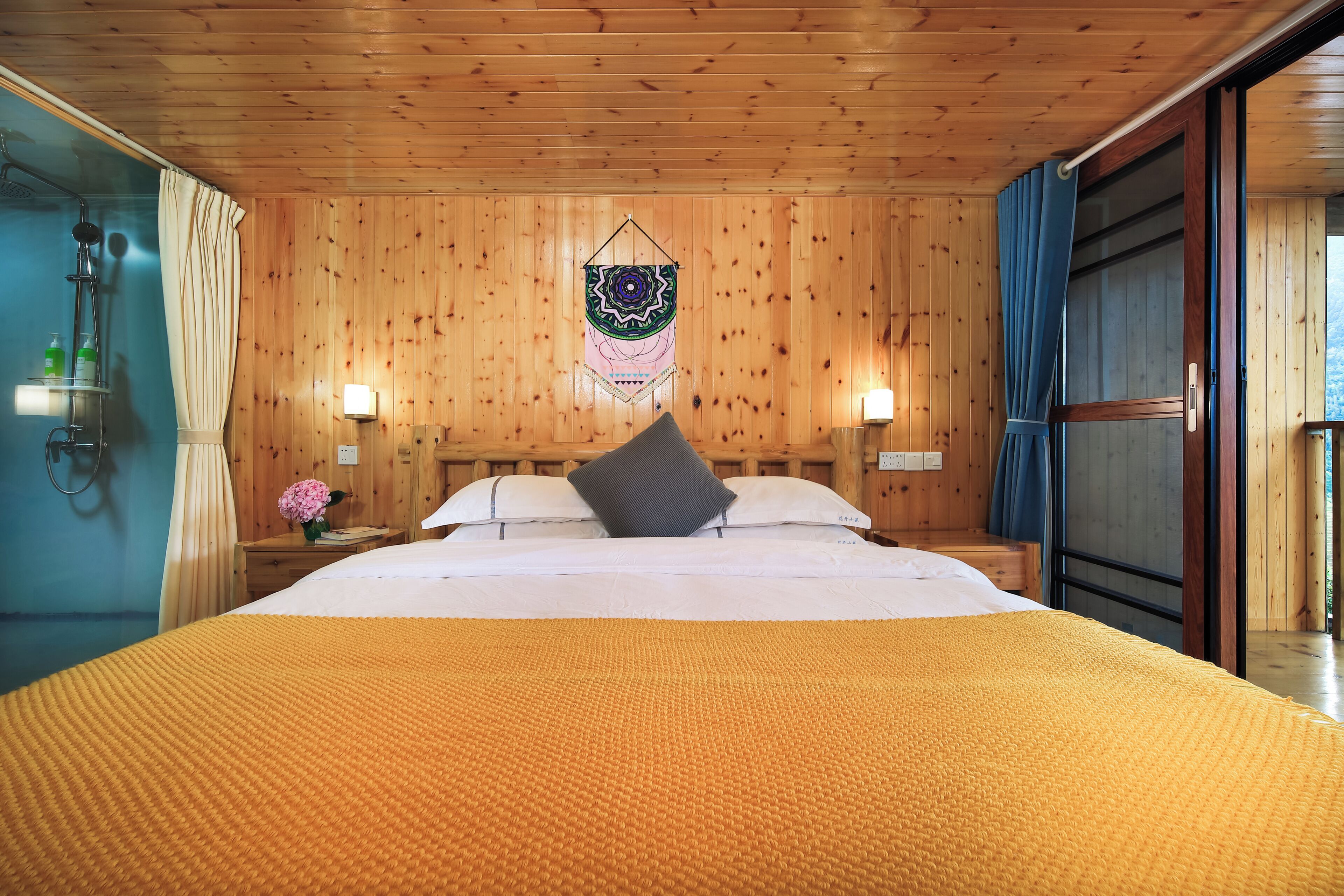 A wooden-paneled room with a bed, two bedside lamps, a wall hanging, and a window with curtains.