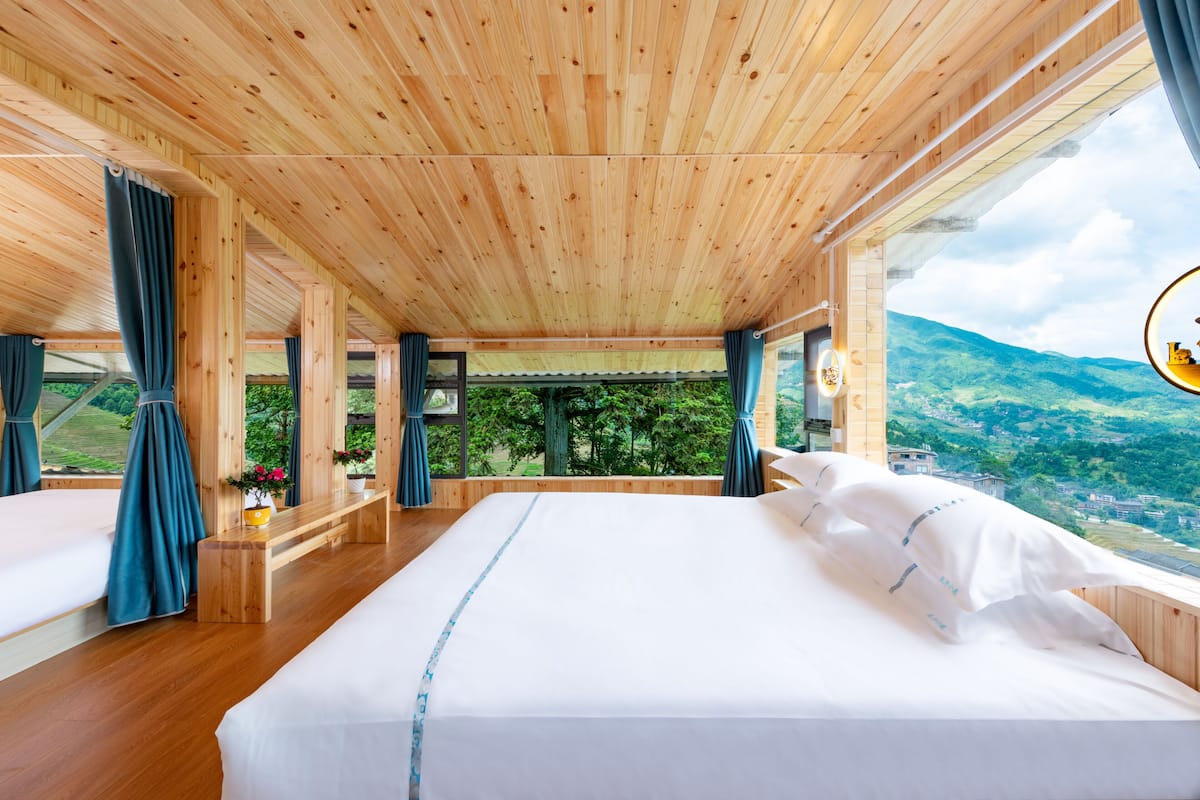 Un dormitorio de cabaña de madera con una cama grande, cortinas y vistas a la montaña.