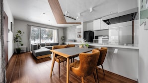 A modern kitchen with a central island, wooden flooring, and a dining area with a table and chairs. - THE VELORA (Asahikawa)