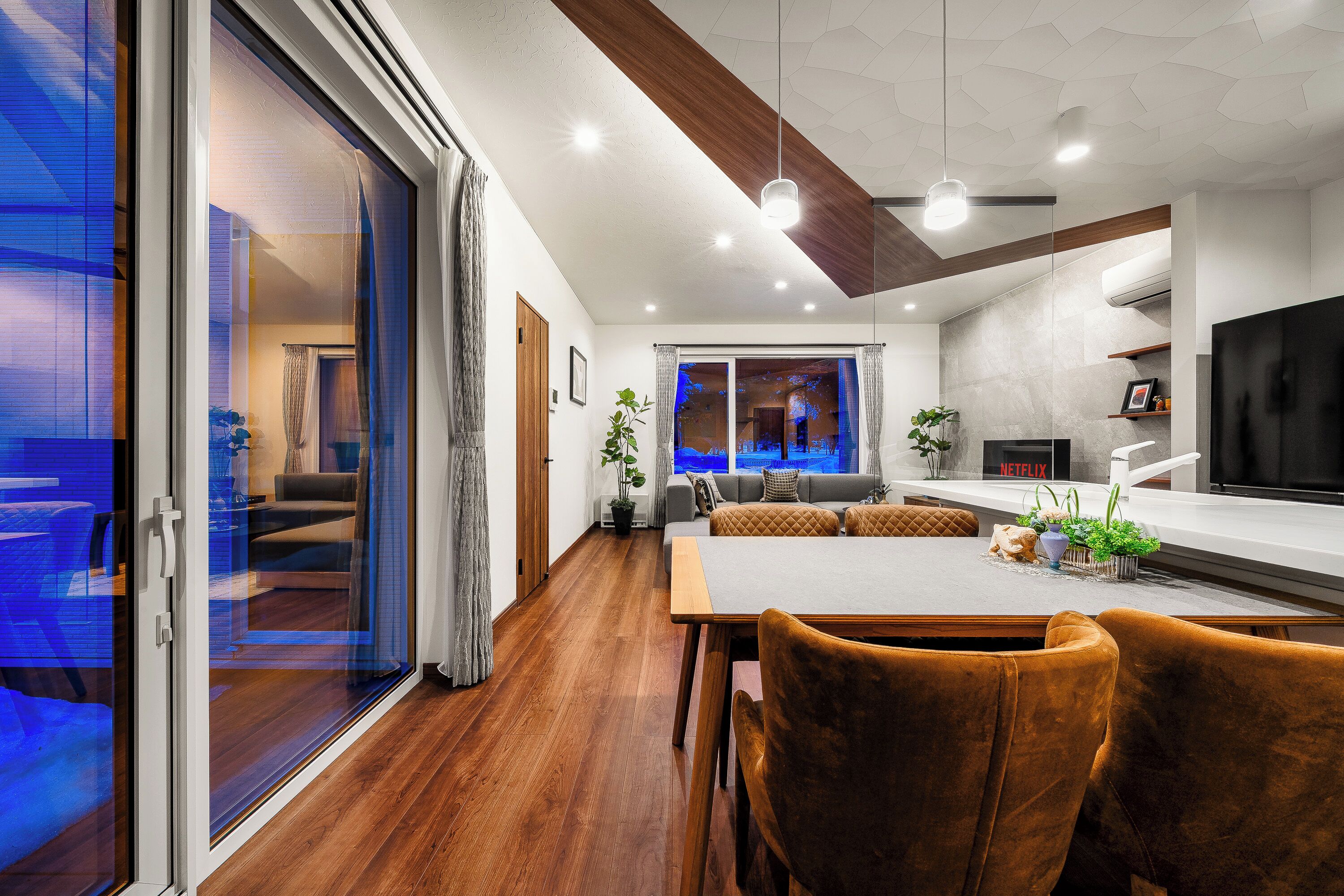 Una sala de estar moderna con comedor, un sofá, un televisor y un amplio ventanal con cortinas.