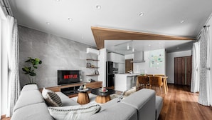 A modern living room with a grey sofa, wooden coffee table, and a TV displaying Netflix. - THE VELORA (Asahikawa)