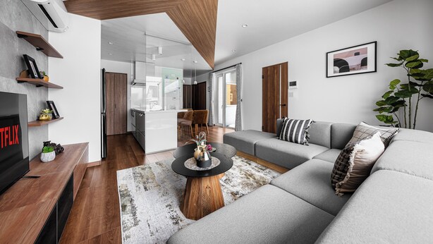 A modern living room with a sofa, coffee table, and TV. There is a kitchen area in the background. - THE VELORA (Asahikawa)