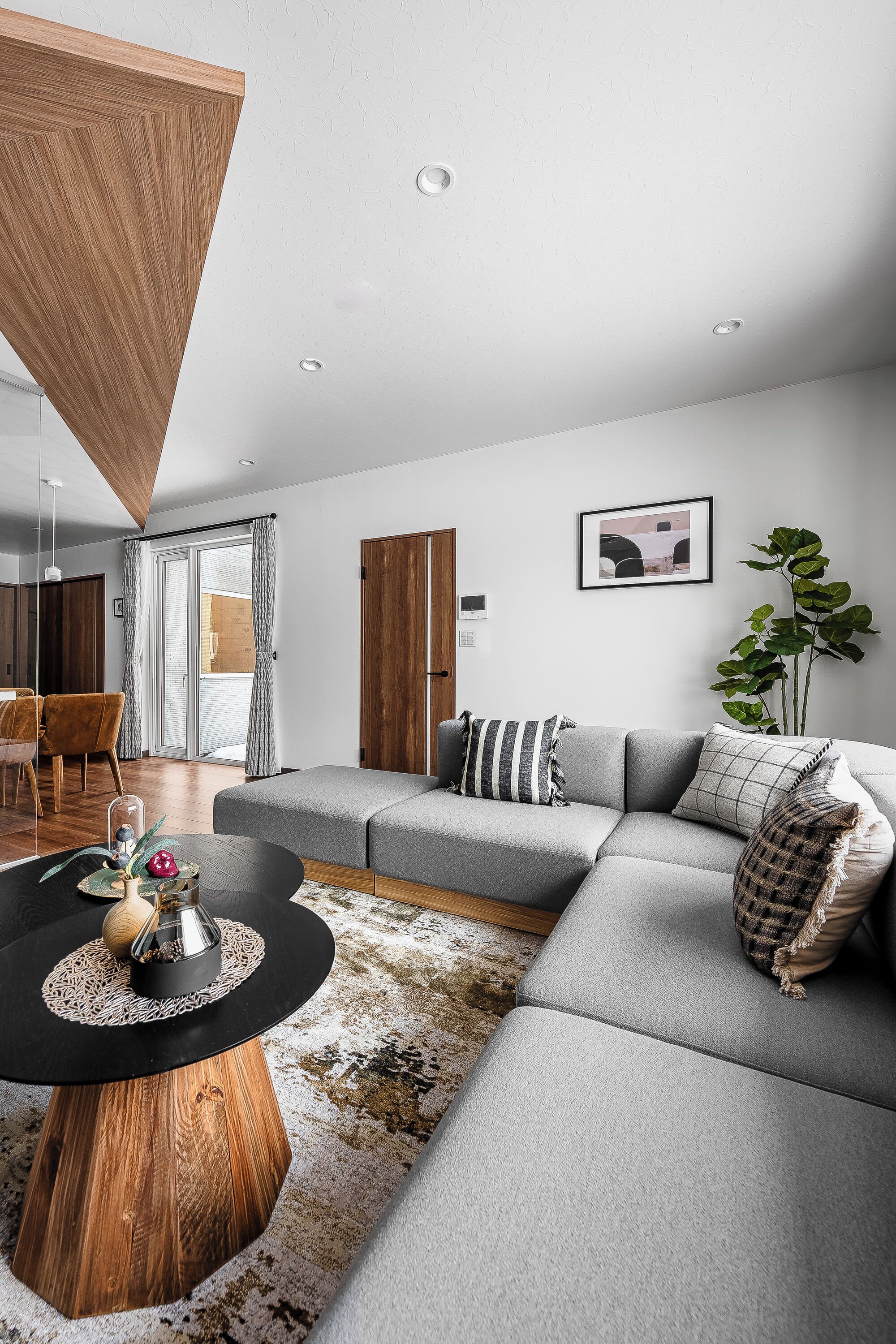 A modern living room with a grey sectional sofa, a wooden coffee table, and a large plant.