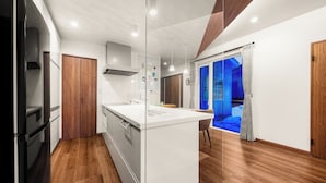 A modern kitchen with a central island, wooden flooring, and a view into a living area. - THE VELORA (Asahikawa)