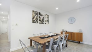 A dining area with a wooden table, metal chairs, a clock, and artwork on the wall.