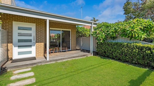 A residential property with a brick facade, a sliding glass door entrance, a covered patio area, and a well-maintained lawn.