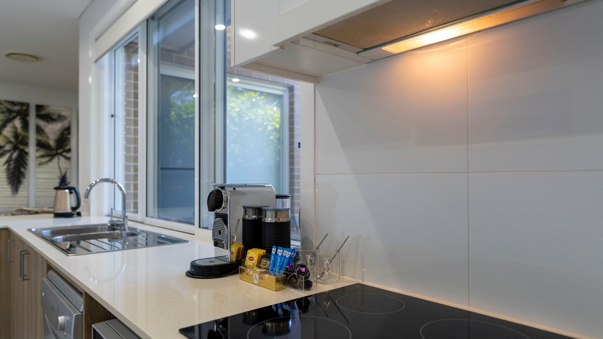 Une cuisine moderne équipée d’une cuisinière intégrée, d’une machine à café et d’une fenêtre donnant sur un espace verdoyant.